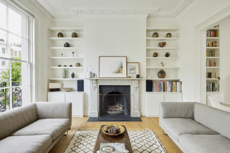 The living room, with grey sofas opposite one another, a central fireplace and bookshelves in the alcoves.